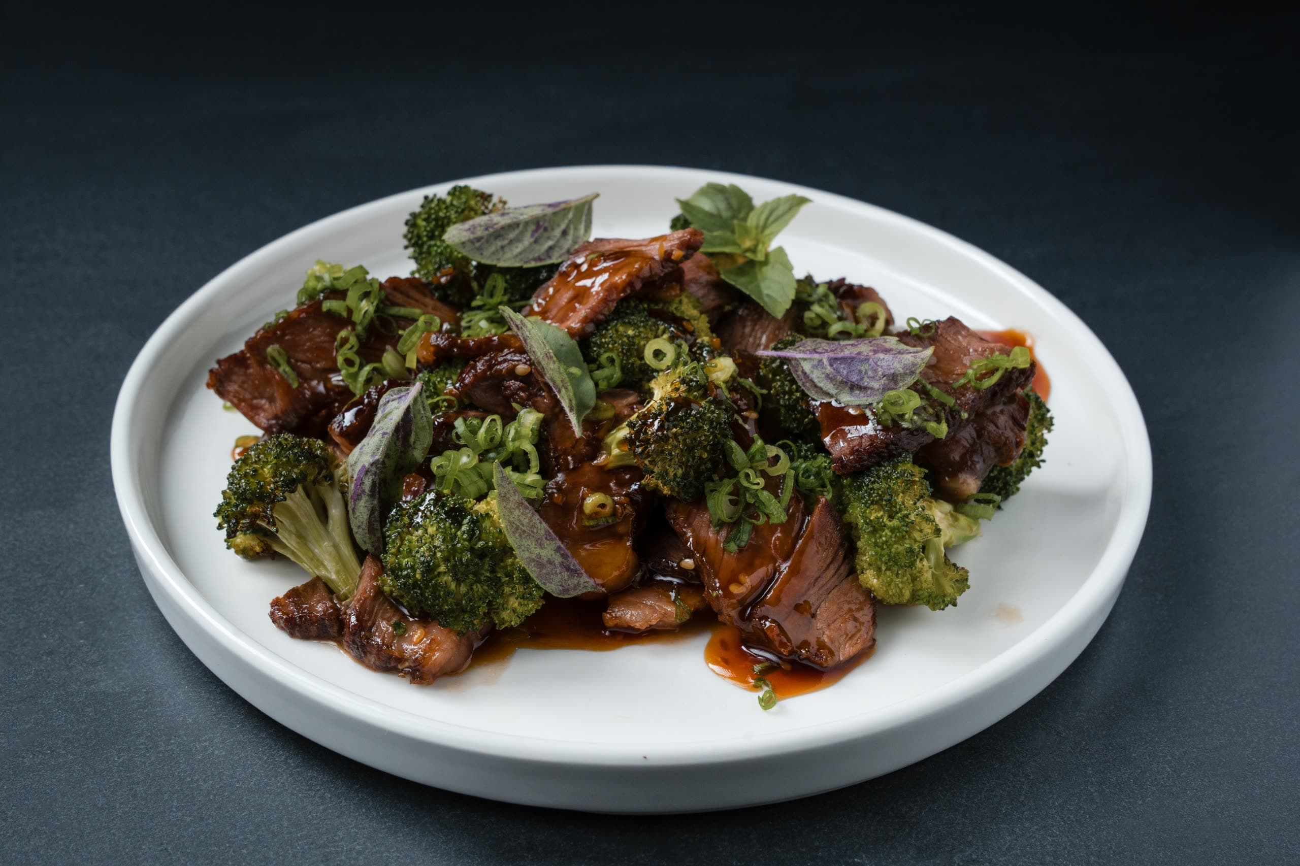 Glazed beef and roasted broccoli under scallion and chili, plated on a white dish