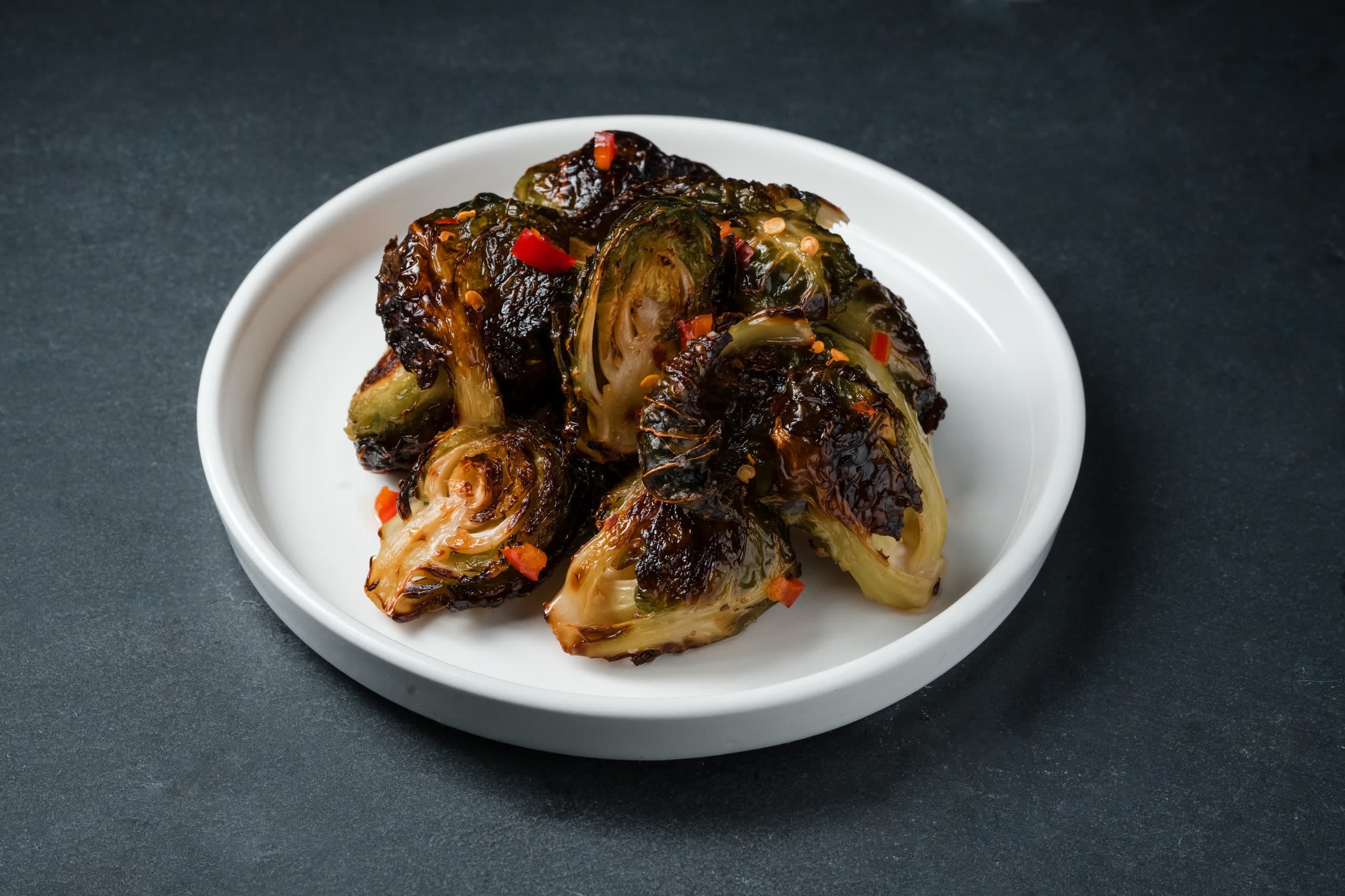 Charred brussels sprouts with chili and citrus, plated on a white dish