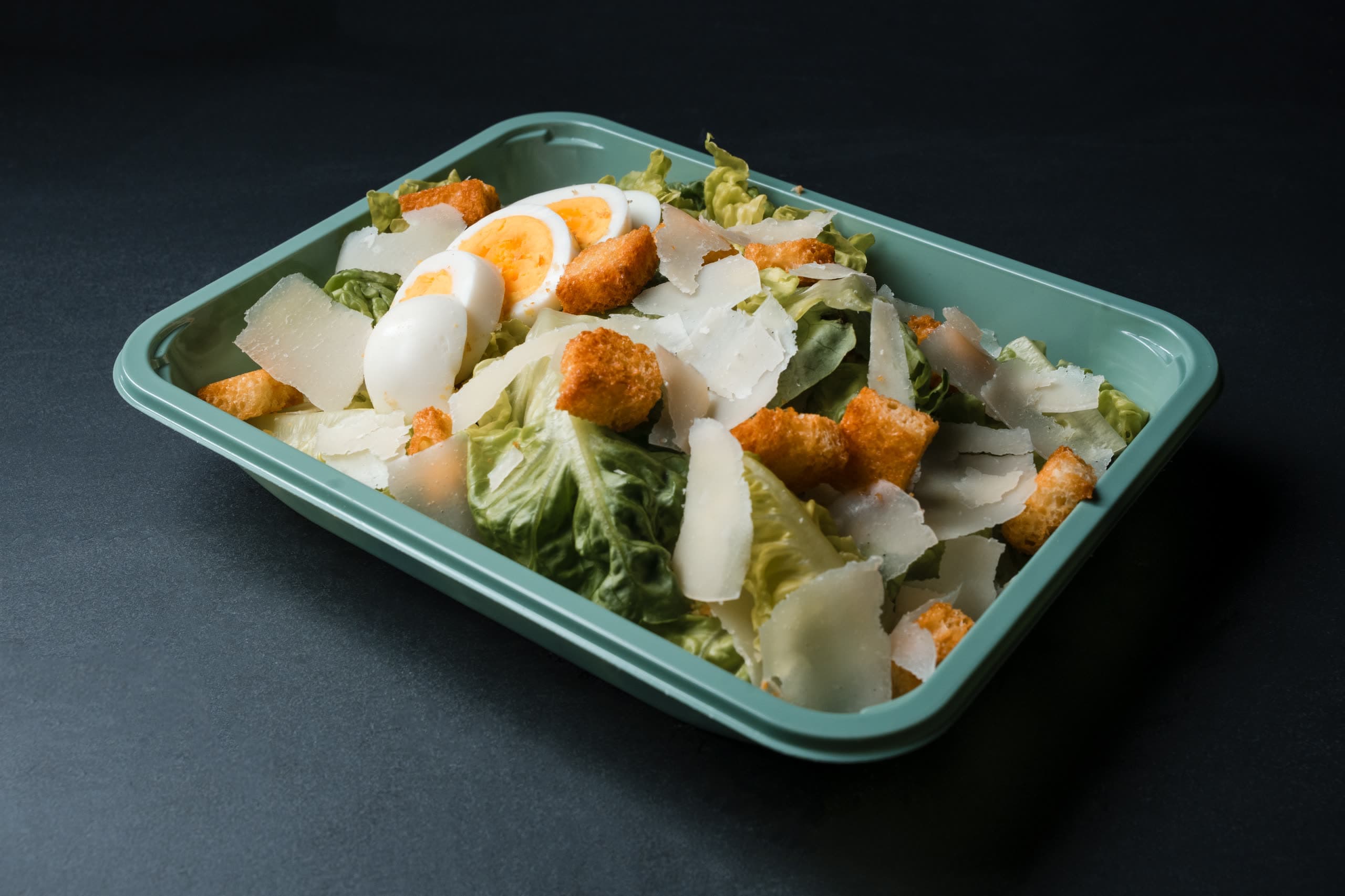 Caesar salad with shaved parmesan, croutons, and a halved egg in a sage-green ABLTY tray
