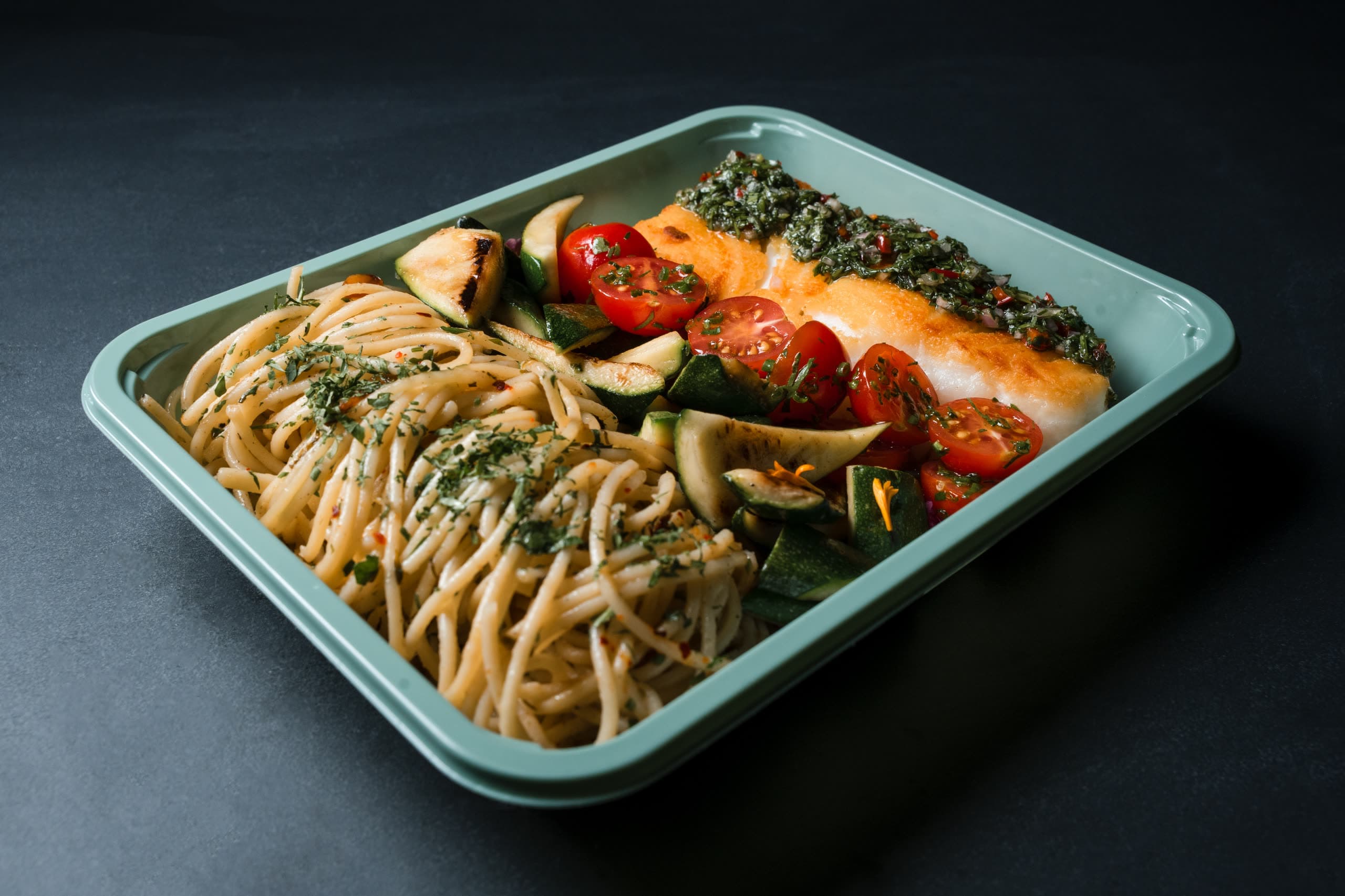 Herb-crusted cod with blistered tomatoes, zucchini, and whole-grain spaghetti in a sage-green ABLTY tray