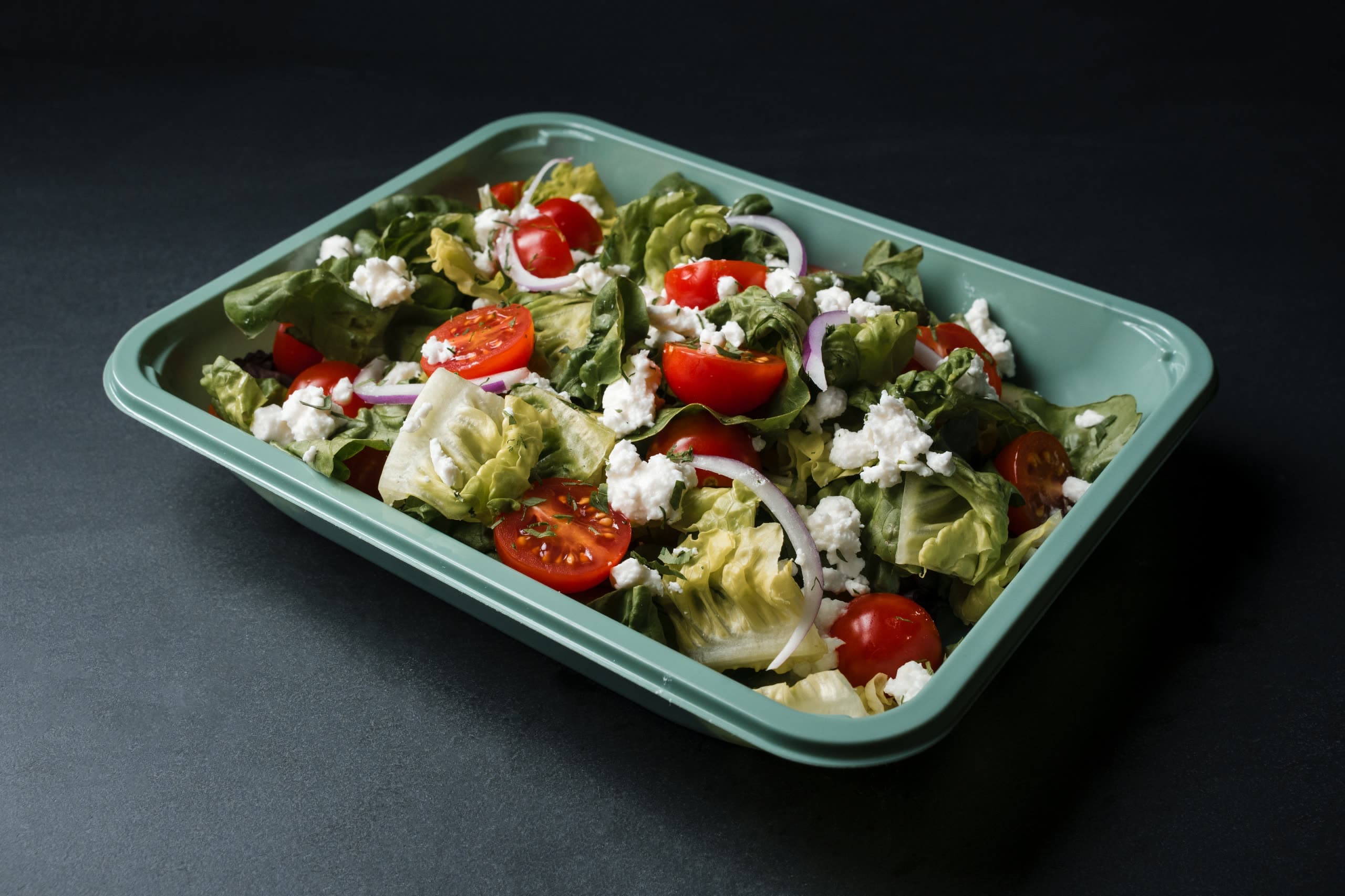 Chopped Greek salad with cherry tomatoes, red onion, and feta in a sage-green ABLTY tray