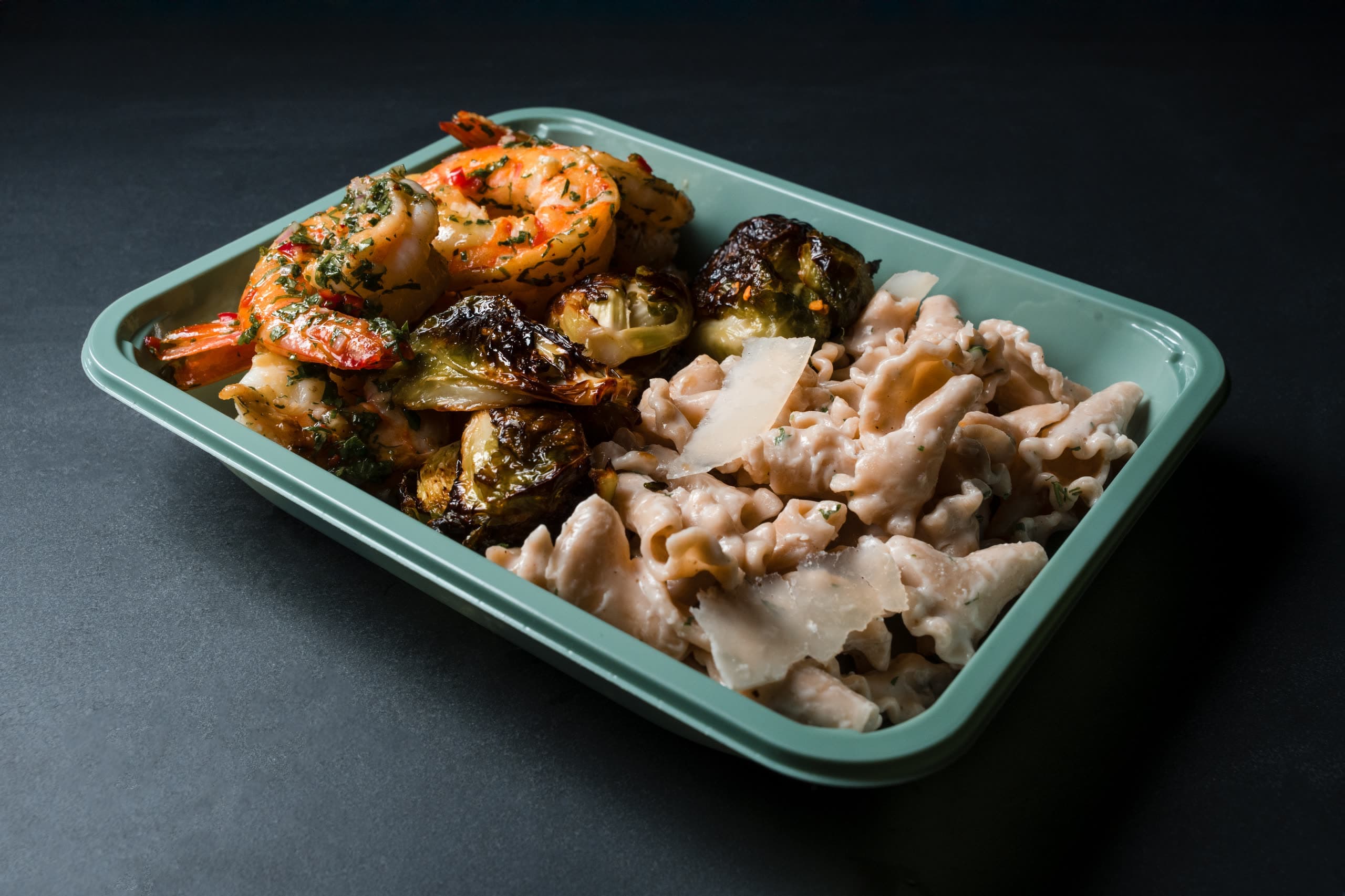 Shrimp with charred brussels sprouts and creamy shell pasta with shaved parmesan in a sage-green ABLTY tray