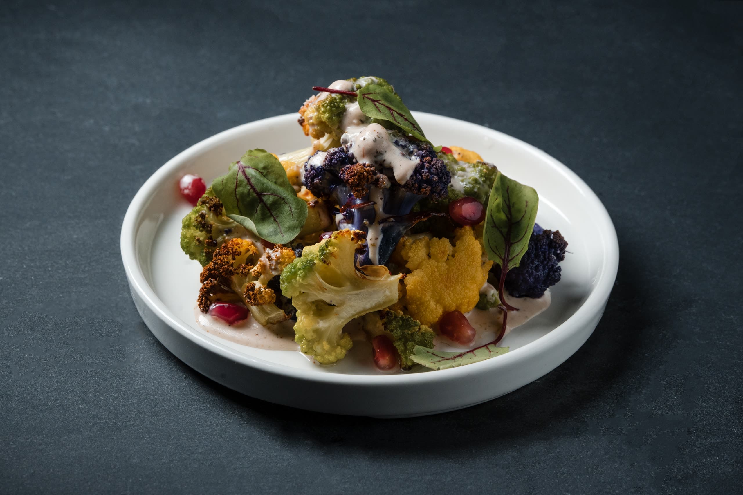 Roasted cauliflower in three colors with tahini, pomegranate seeds, and red-veined sorrel, plated on a white dish