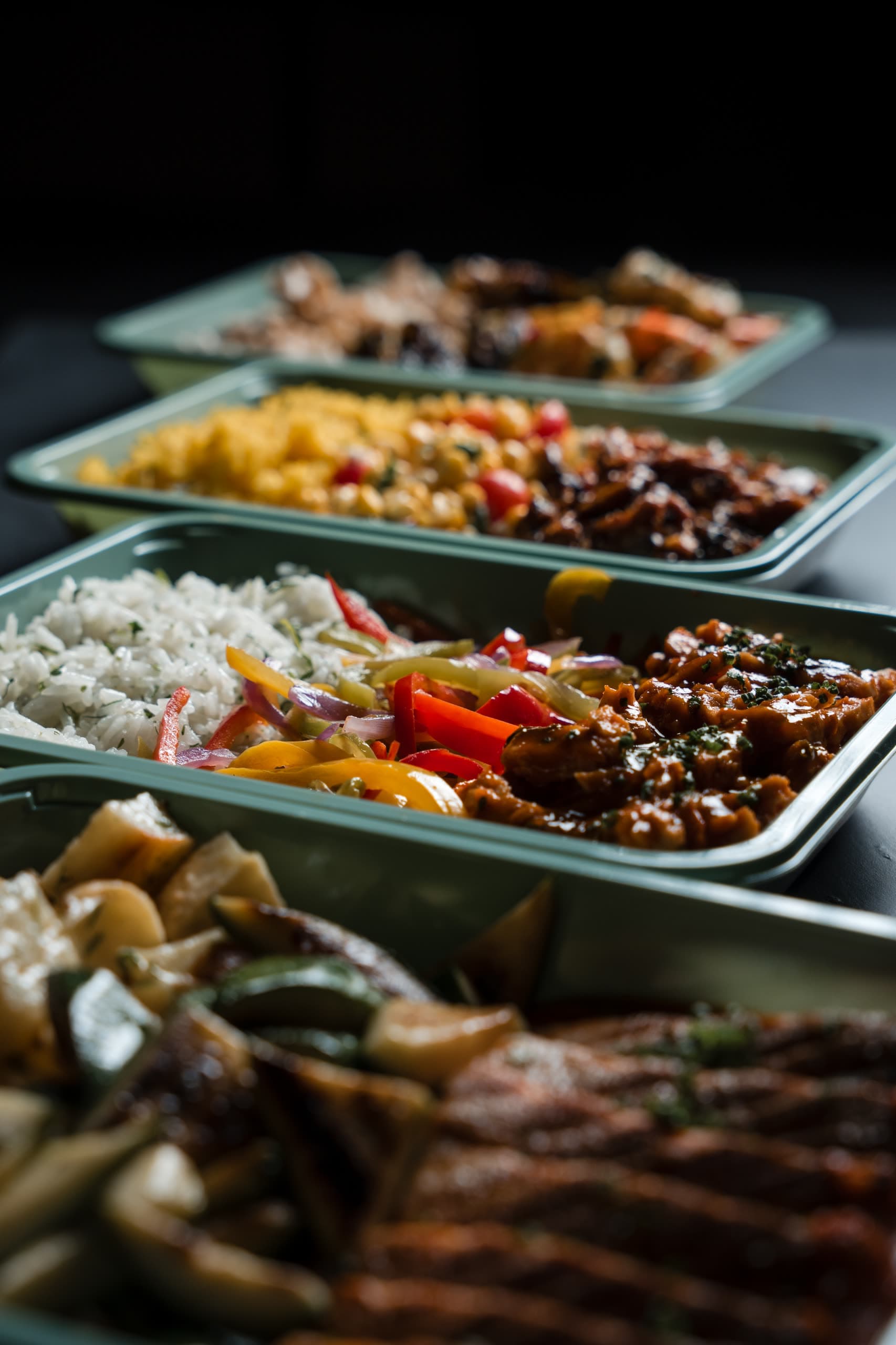 A line of ABLTY meal trays, herbed rice, sautéed peppers and braised chicken sharp in the tray at centre