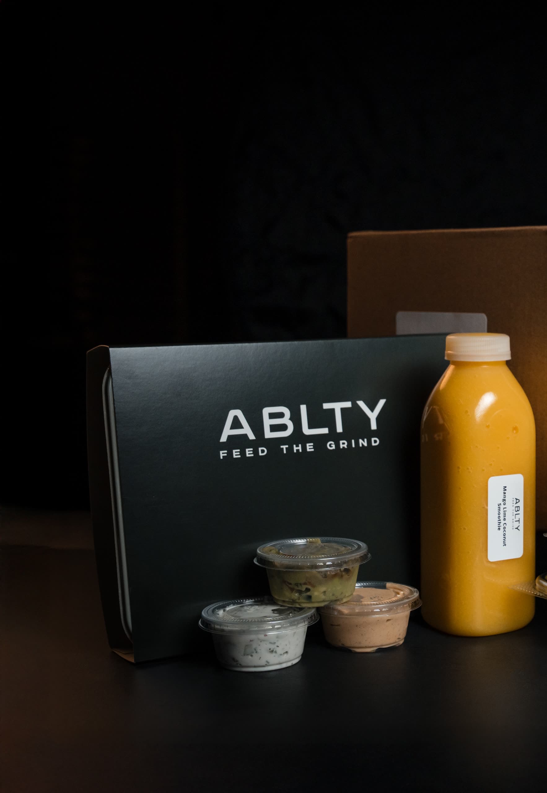 A packed ABLTY order — black insulated mailer, kraft box, stacked meal sleeves, a smoothie bottle and sauce cups