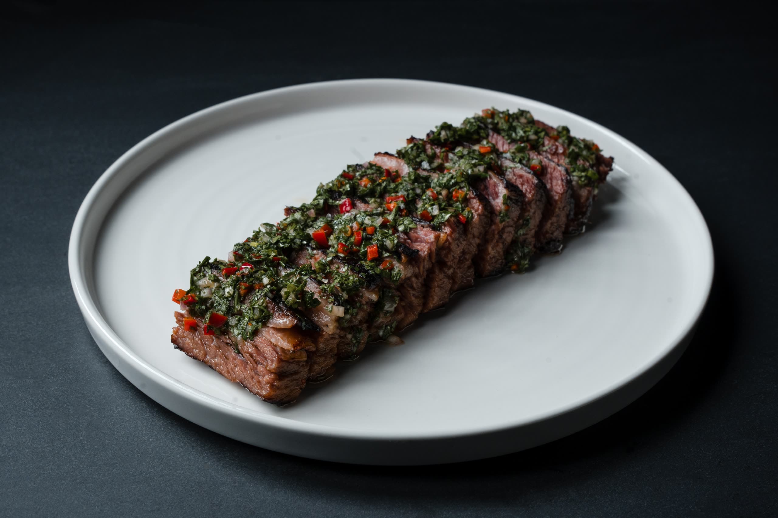 Sliced steak under a chimichurri crust, plated on a white dish in the ABLTY commissary
