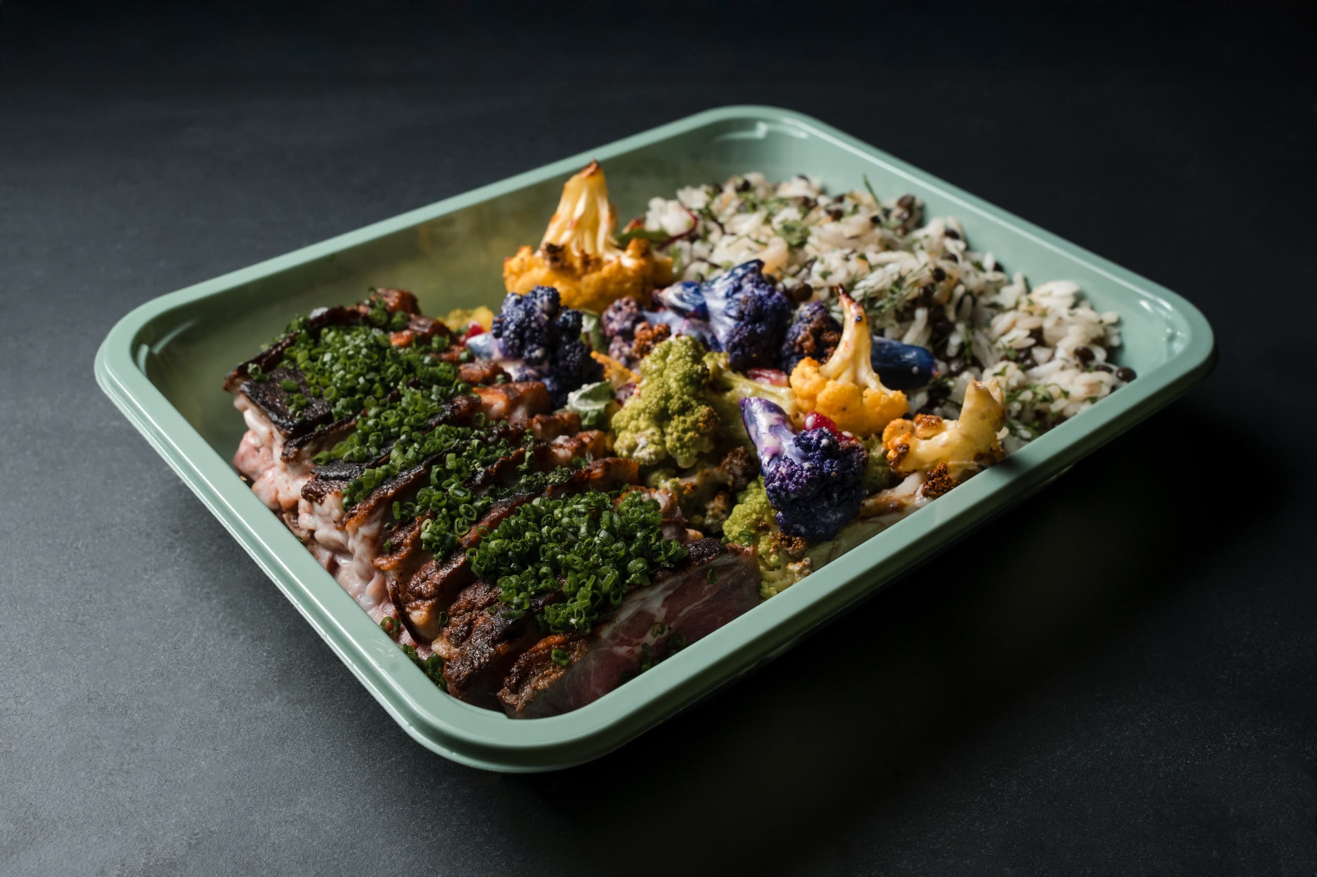Sage-green ABLTY travel tray holding sliced chimichurri short rib, roasted cauliflower, and herbed rice