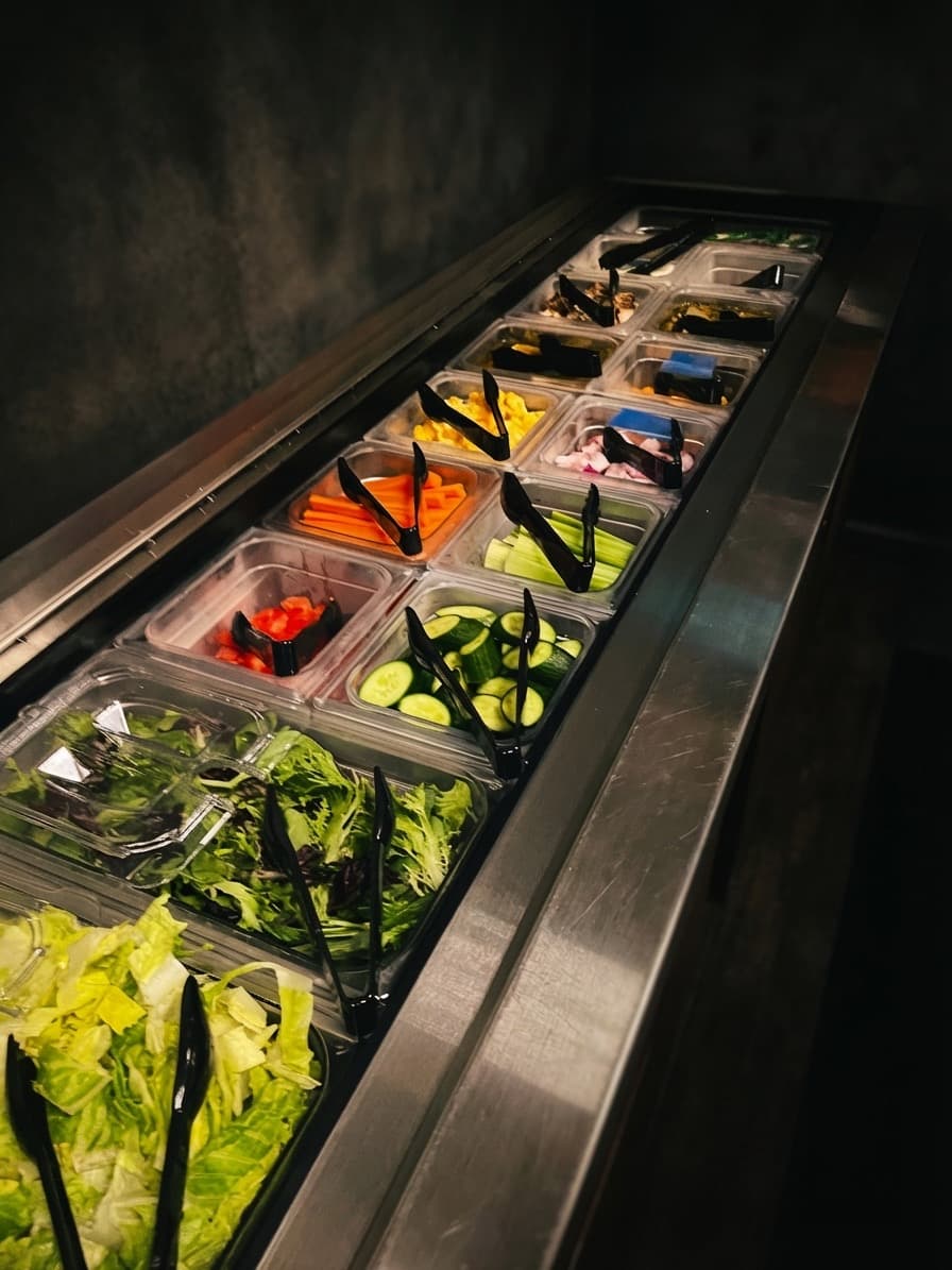 Fresh vegetable salad bar station with lettuce, cucumbers, carrots, and peppers in hotel pans