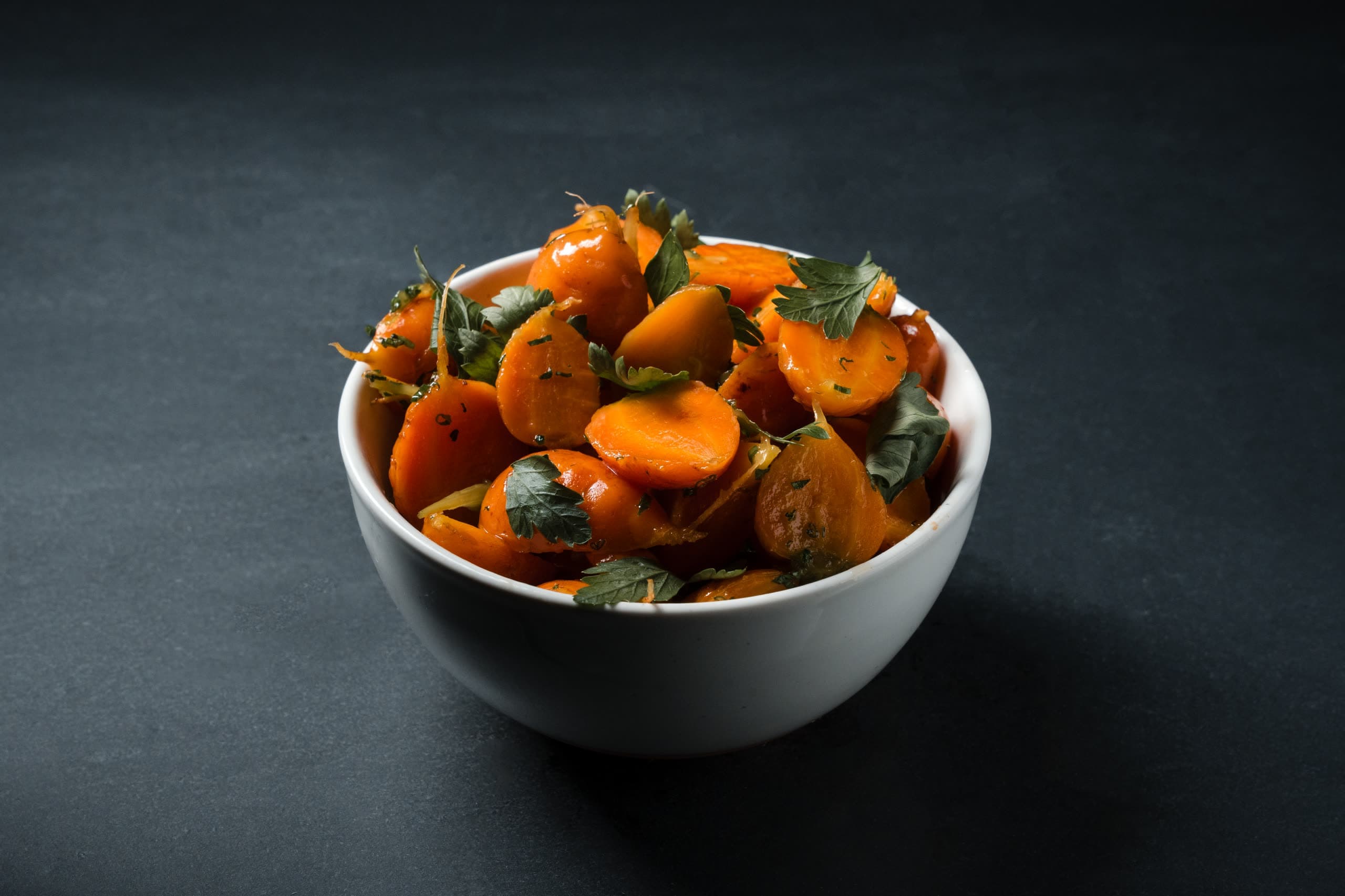 Glazed carrot coins with parsley in a white bowl