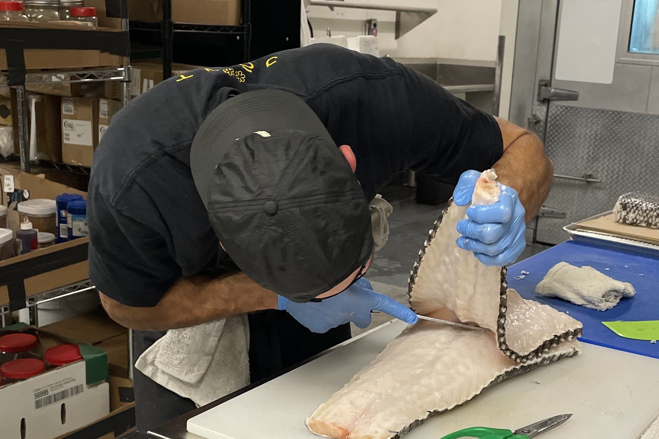 Chef in black prepping fish at a cutting board in ABLTY commercial kitchen