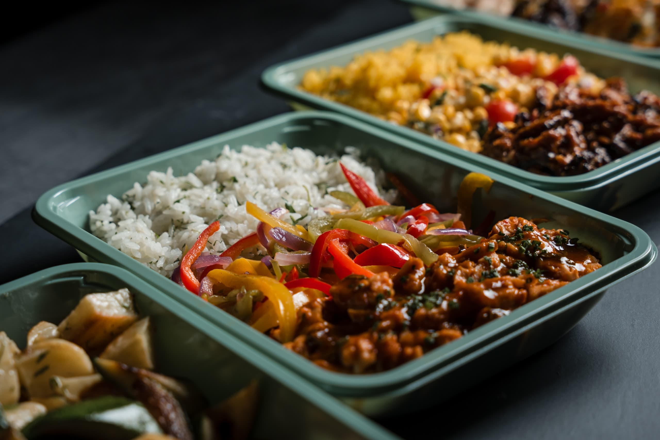 A line of sage-green ABLTY trays holding herbed rice, peppers, and stewed meat
