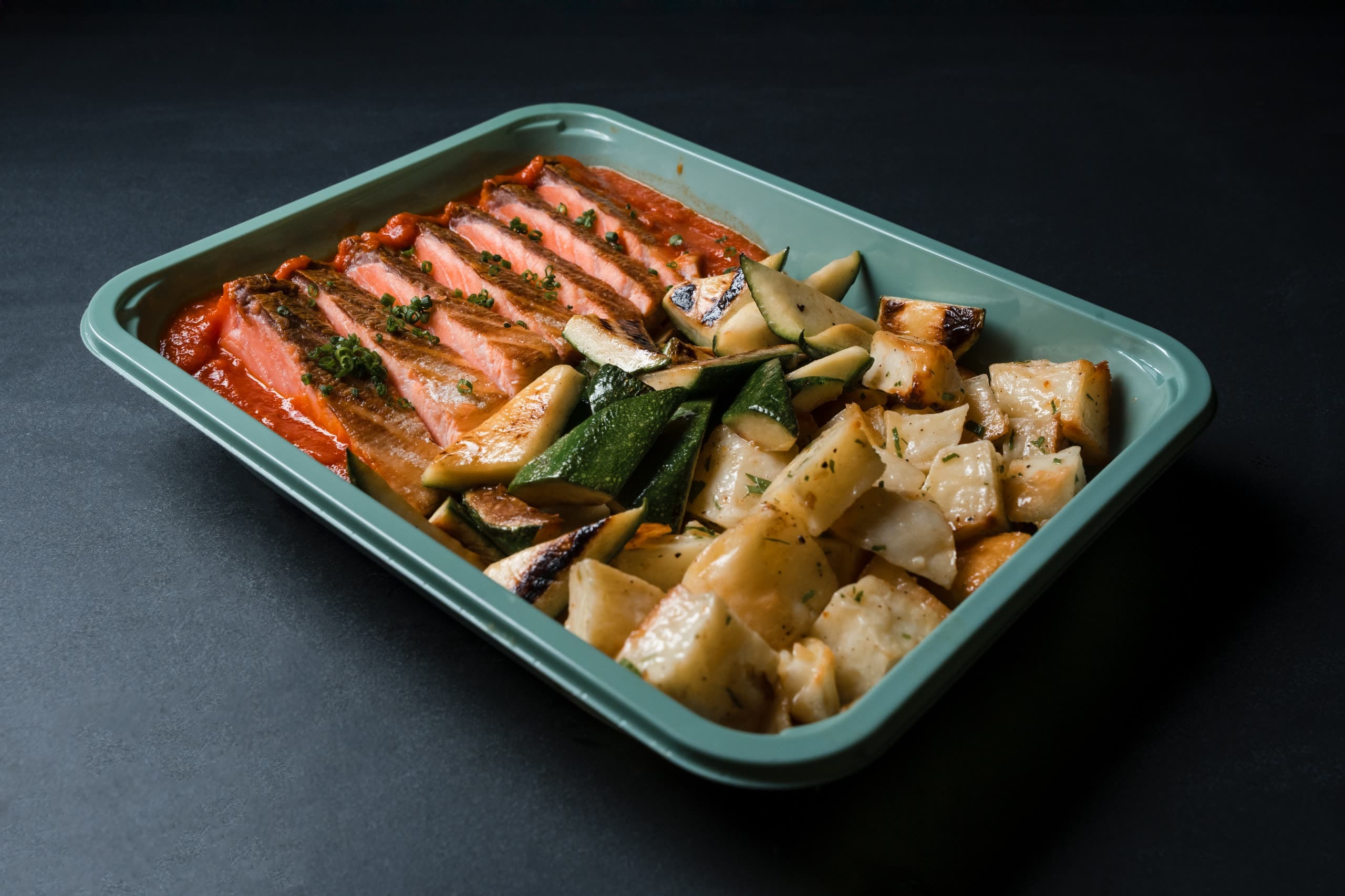 Seared salmon over romesco with charred zucchini and roasted potatoes in a sage-green ABLTY tray