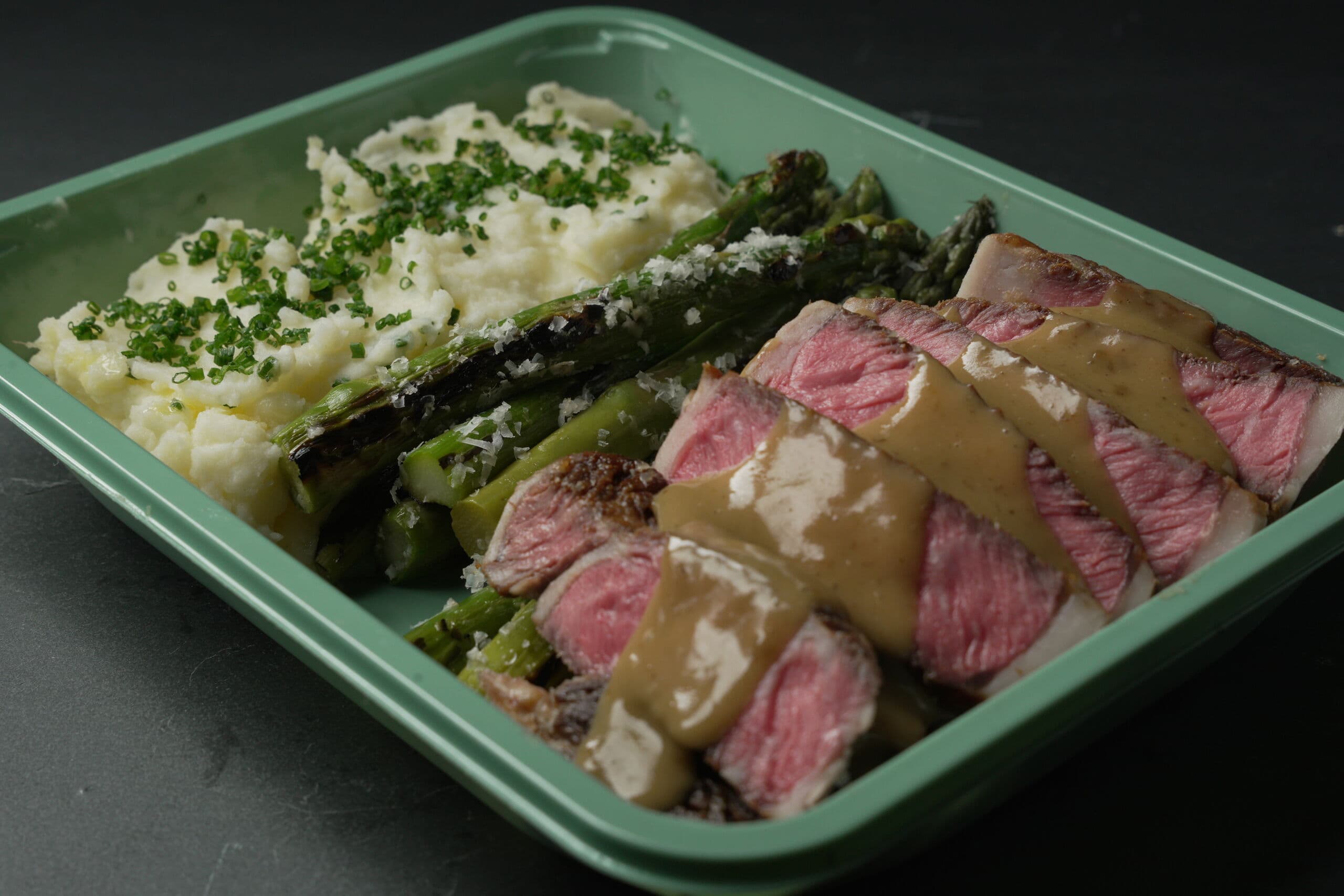 Sliced strip steak with peppercorn sauce, charred asparagus and whipped potato in an ABLTY service tray